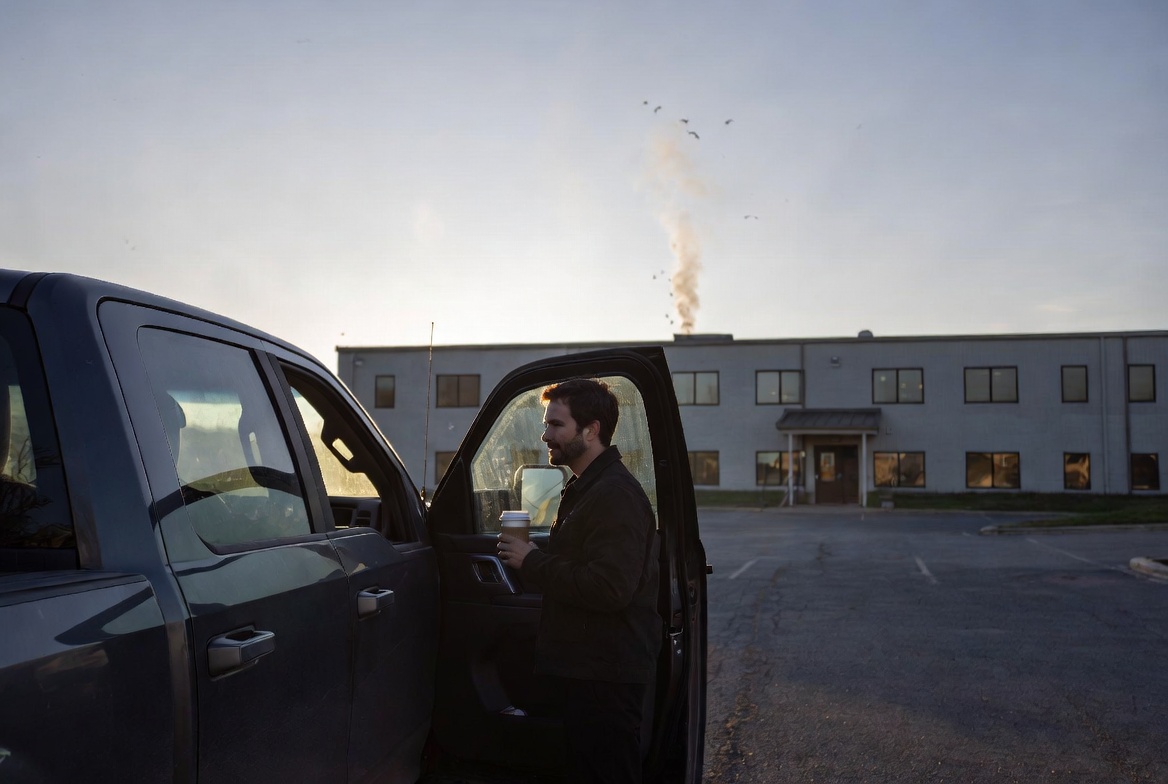 Joe steps out of his truck, coffee in hand, smoke rising behind the building